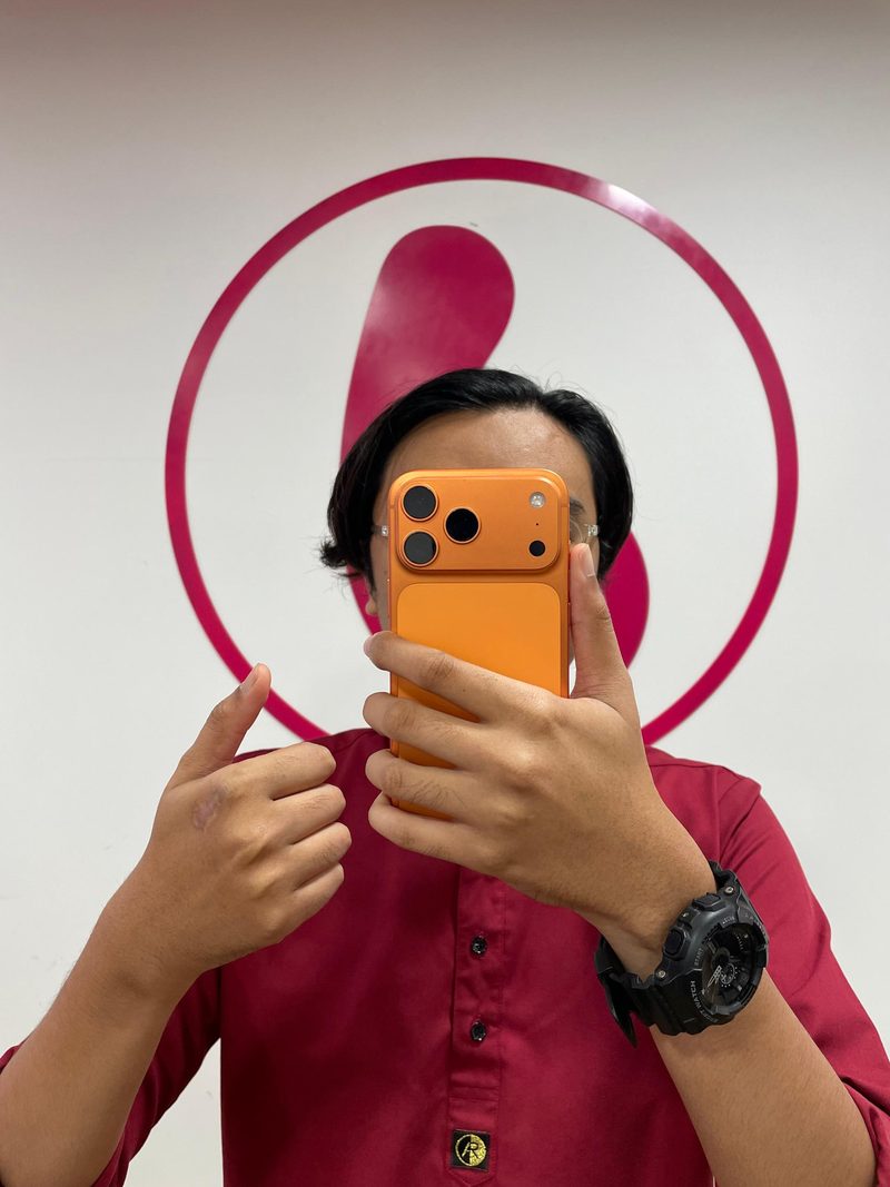 A bright orange iPhone held up in front of the Berry Nice brand wall in Sentul, KL
