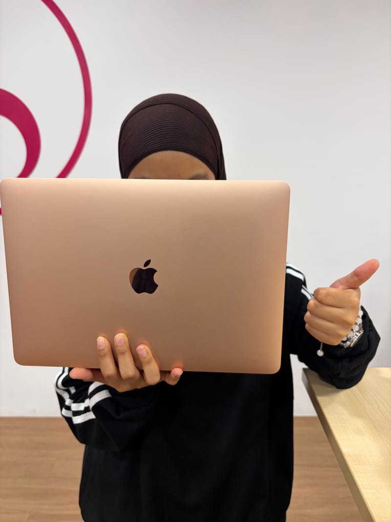 Berry Nice staff holding a rose gold MacBook Air for inspection in front of the brand wall